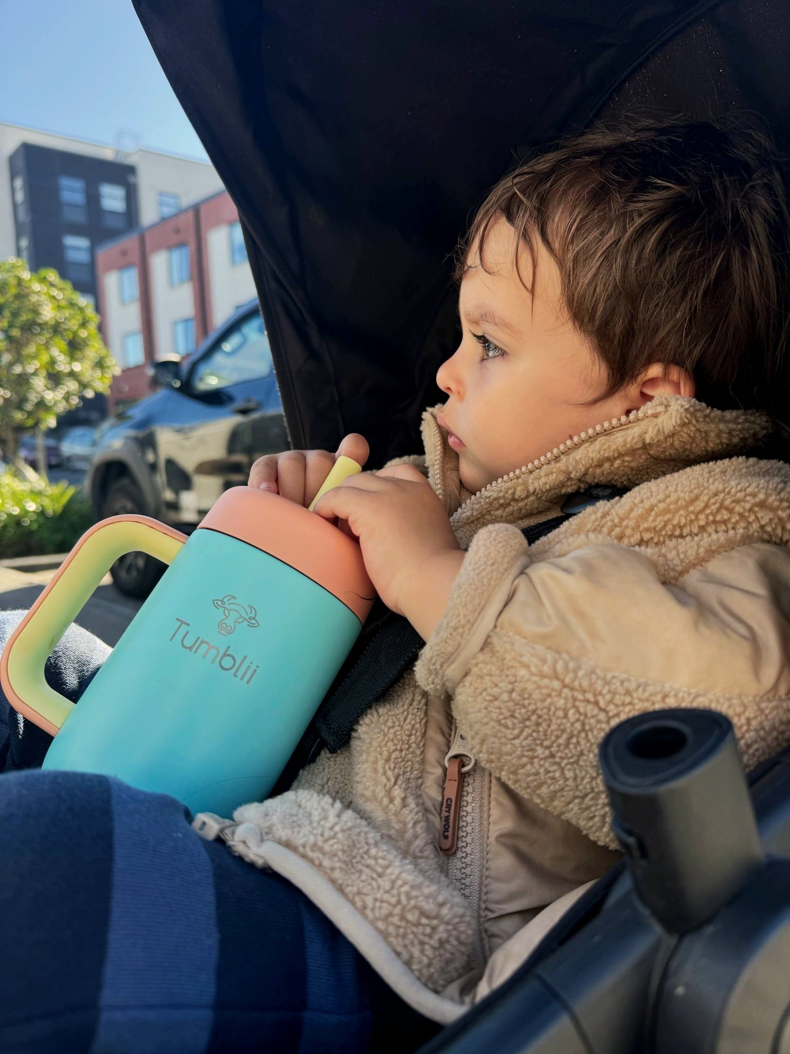 Toddler holding blue tumblii tumbler straw cup in pram